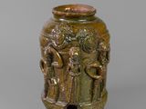 an old bronze vase with figures on it on a gray surface