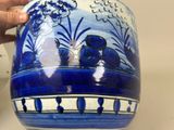 a person holding a blue and white vase on a table