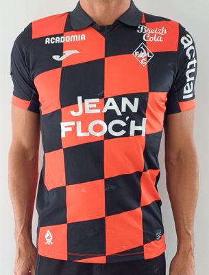 Cet homme porte un t-shirt rouge et noir et un pantalon noir.