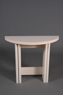 une table en bois blanche au plateau incurvé, sur fond gris