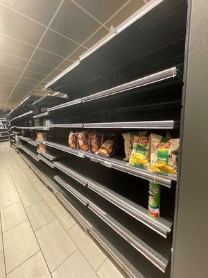 de nombreuses étagères vides dans un supermarché, sur lesquelles se trouvent des produits alimentaires