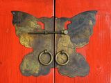 a butterfly shaped door handle on a red wooden door