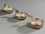 trois plats en argent accompagnés de cuillères, posés sur une table devant un fond gris