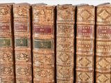 several old books are lined up in a row on a shelf