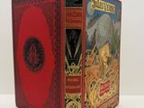 an old book with a red cover sitting on top of a white table