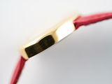 close up of a gold watch with a red leather strap