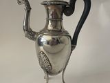 a silver tea pot on a stand with a black handle