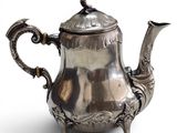 an antique silver tea pot with a bird on top of it