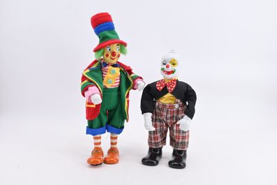 two clown figurines standing next to each other on a white surface