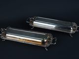 two silverplated rectangular trays with handles on a black background