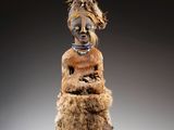 une statue représentant une femme vêtue d'une robe marron et coiffée de plumes
