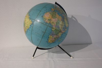 un petit globe bleu posé sur un socle noir, sur une surface blanche