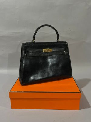 sac à main en cuir noir posé sur une boîte orange sur fond blanc