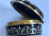 une boîte noire et dorée avec un couvercle, posée sur une surface blanche