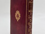 an old red book with gold trim sitting on top of a white surface