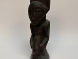 une sculpture noire représentant une femme tenant un vase posé sur une table