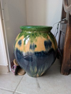 un vase vert et bleu posé par terre près d'un mur