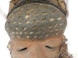 un masque en bois posé sur une surface blanche, entouré d'un fil métallique
