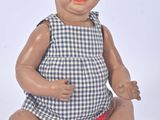 a baby doll sitting on the floor with a blue and white checkered dress