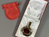 un flacon de parfum dans un étui rouge avec une pochette rouge, posé sur une surface grise