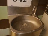 a metal sink in a public restroom with a sign on the wall