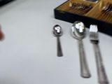 a box of silverware on a table with a knife, spoon, and spoon rest