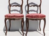 pair of antique chairs with red upholstered cushions against a white wall