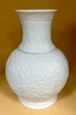 a white vase sitting on a table with a yellow wall in the background