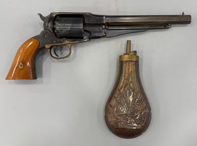 un vieux revolver et une petite fiole en laiton posés sur une surface blanche