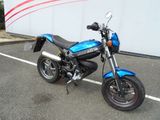 une moto bleue garée sur un parking, près d'un mur