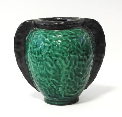 un vase vert muni d'une anse noire, posé sur une surface blanche