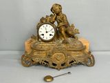 une horloge en or posée sur une table, à côté d'une cuillère