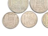 six silver coins of different shapes and sizes on a white surface