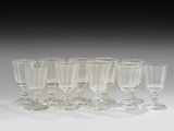 six verres à vin transparents sont alignés sur une surface blanche