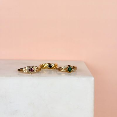 a close up of three gold rings with green and red stones on a marble block