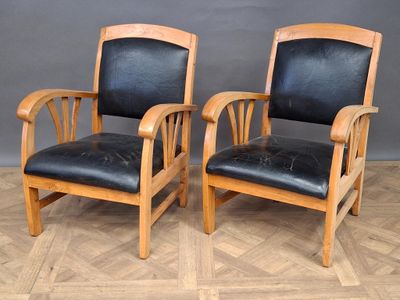 two wooden chairs with black leather upholstered seats on a parquet floor