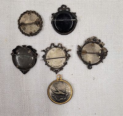 six broches anciennes de formes et de tailles variées, disposées sur un tissu blanc