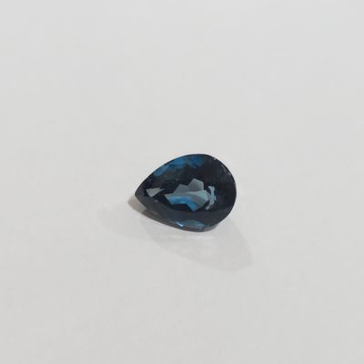 une topaze bleue en forme de poire posée sur une surface blanche