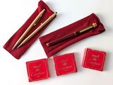 trois boîtes rouges ornées d'une inscription dorée et un stylo dans un étui rouge