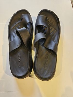 une paire de sandales noires posées sur une surface blanche, avec une bouteille d'eau
