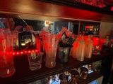 bottles and glasses on a shelf in a bar with red lights