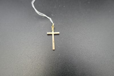 une petite croix en or suspendue à une chaîne en argent sur un fond noir