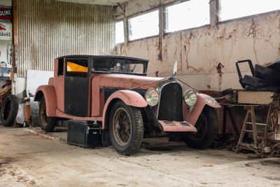 an old pink car parked in a garage with other cars