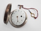 une montre de poche en argent posée sur une table, avec une clé