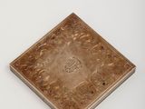 une vieille plaque en laiton ornée d'un motif sur un fond blanc
