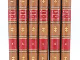 six old books are lined up in a row on a white surface