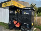 une poubelle noire sur laquelle est dessinée une pizza, à côté d'une clôture blanche
