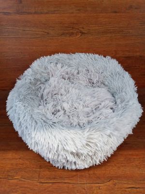 the dog bed is made of fluffy gray fur and sits on a wooden floor