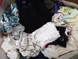 une valise pleine de vêtements et des vêtements posés par terre