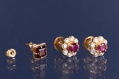 trois paires de boucles d'oreilles à clous en rubis et diamants posées sur une surface réfléchissante